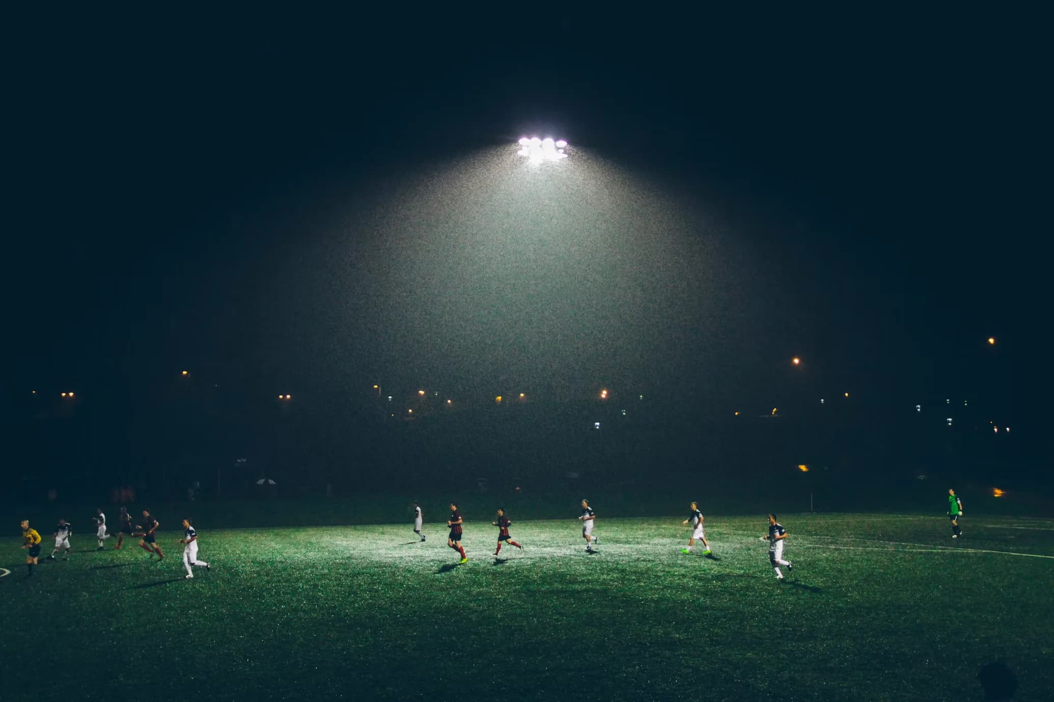 A soccer match under floodlights at night, the lit pitch filling the frame against a dark sky.